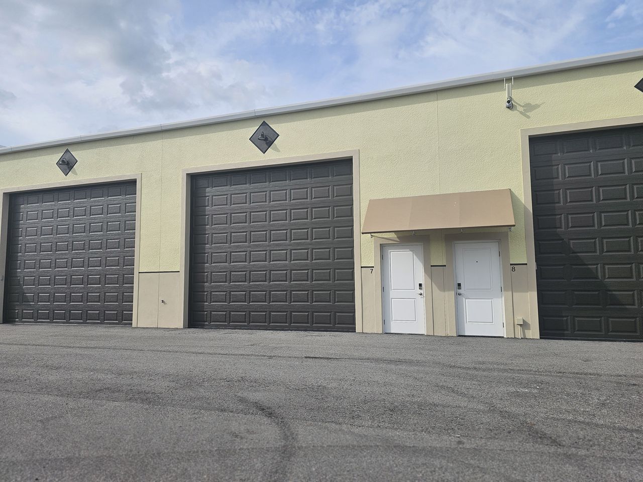 Garage condo building exterior with security camera and wide paved drive